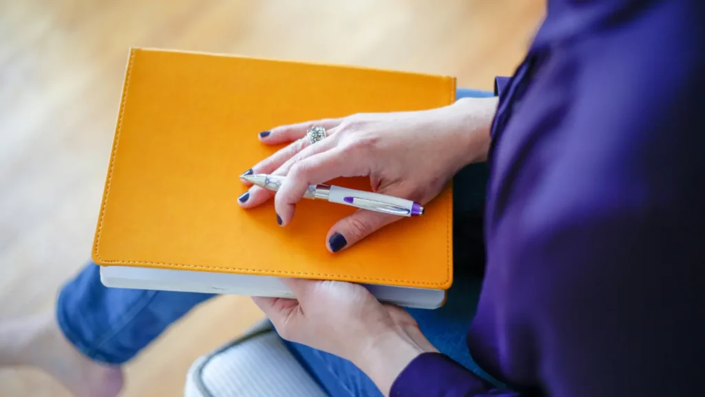 Person writing at a desk with a laptop and notepad